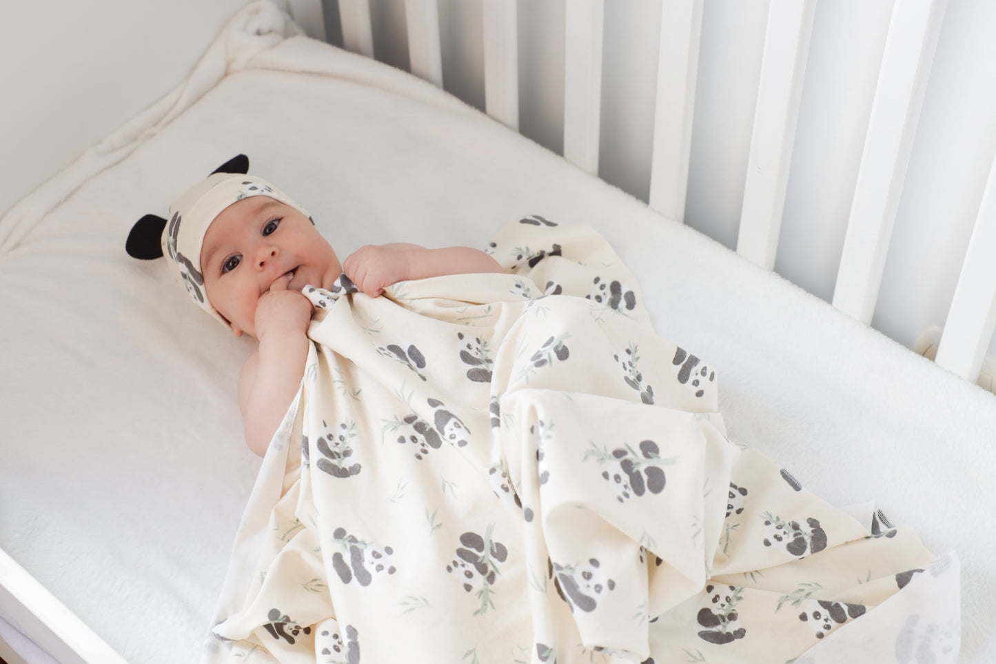 Baby in crib with swaddle blanket and hat